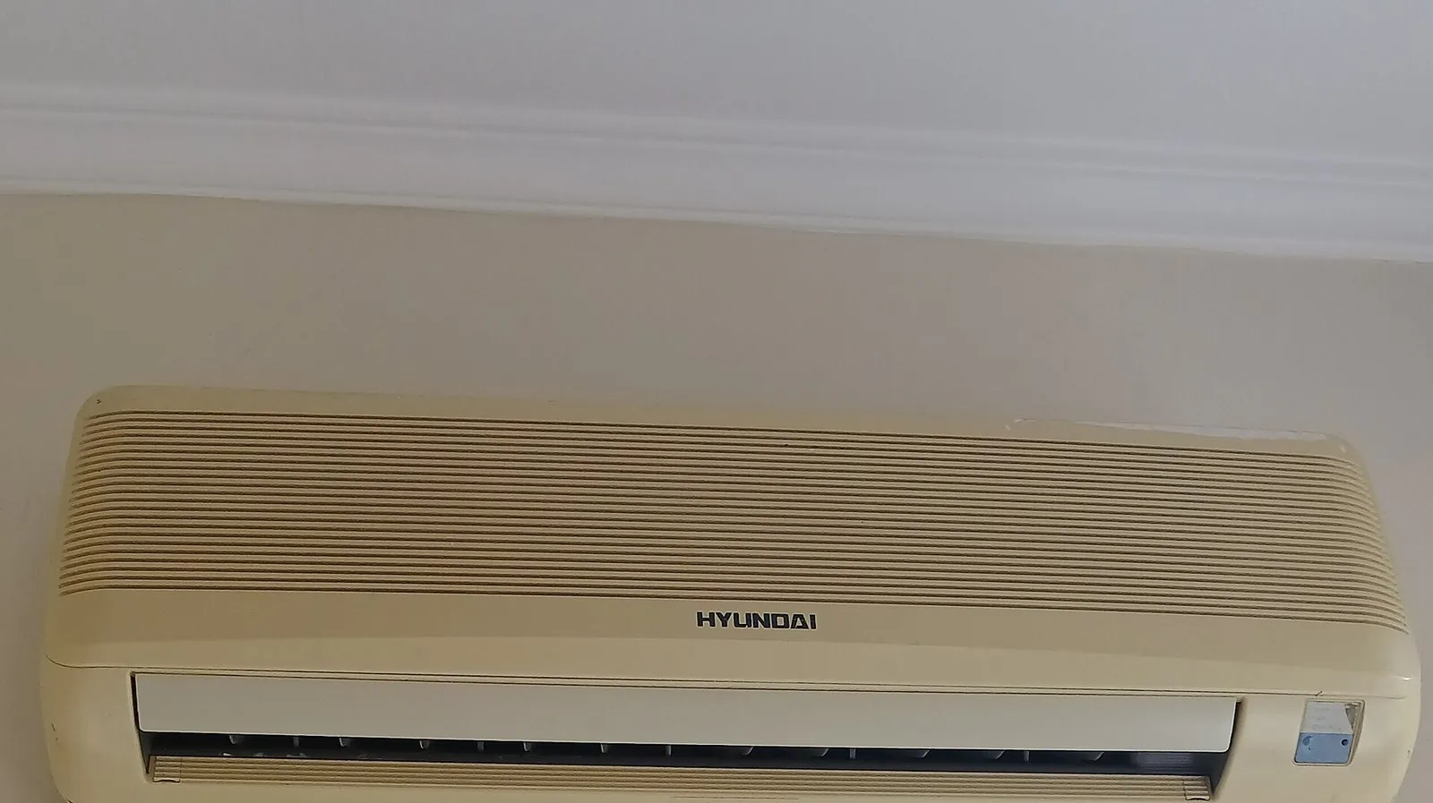 A wall-mounted split air conditioner fixed high on a plain wall