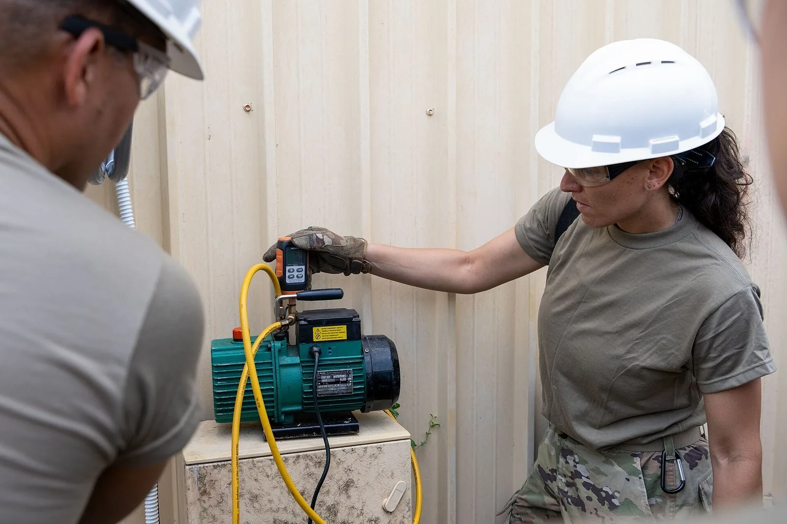 Two technicians running a vacuum pump while fitting an air conditioner